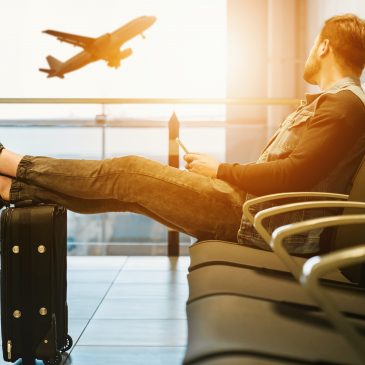 Juego de maletas del Real Madrid. Un hombre sentado en un aeropuerto, se ve un avión de fondo a través de las cristaleras.
